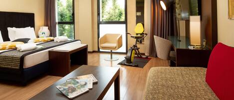 A hotel room with a bed, a desk, a chair, a treadmill, and a TV.
