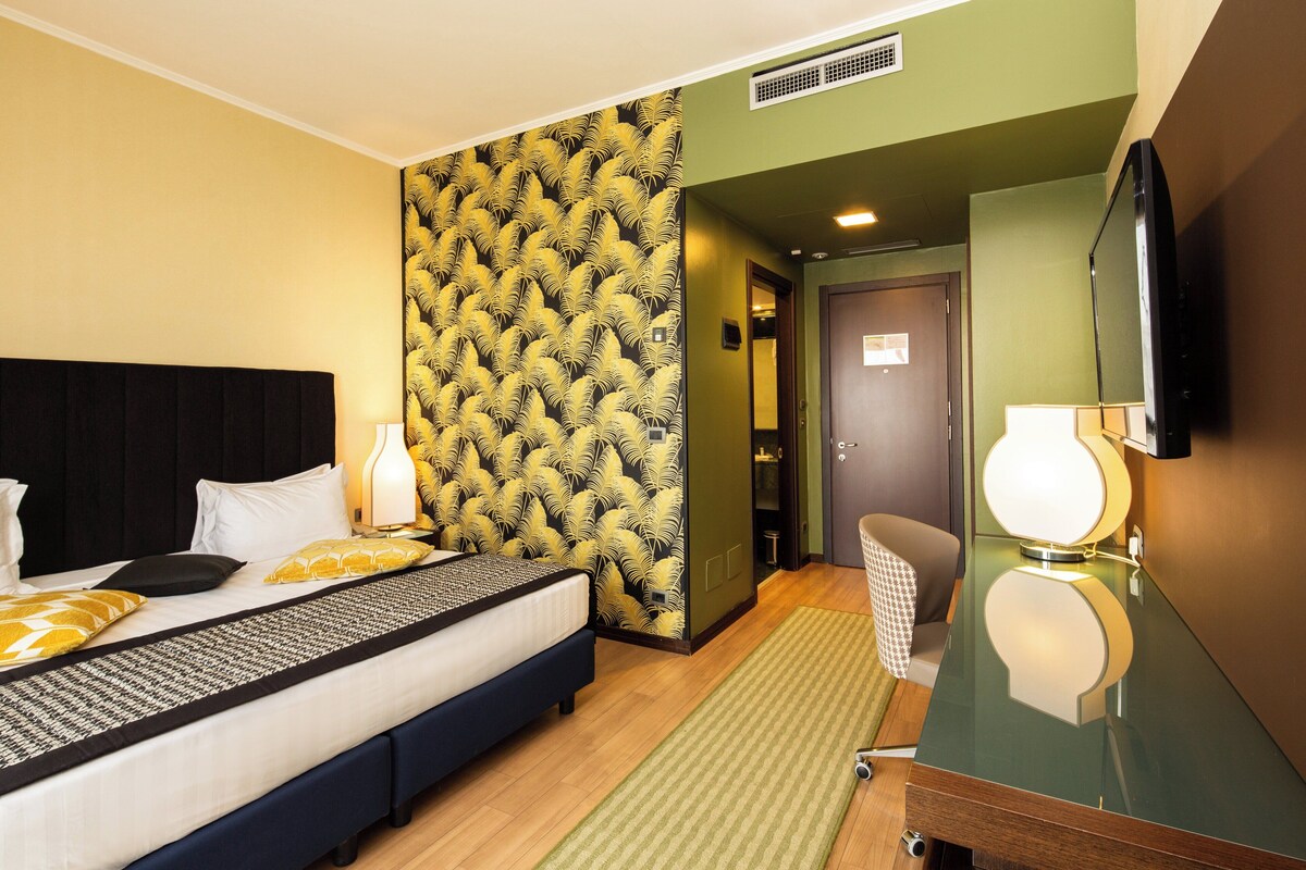 Een hotelkamer met een bed, een spiegel, een televisie en een behang met patroon.