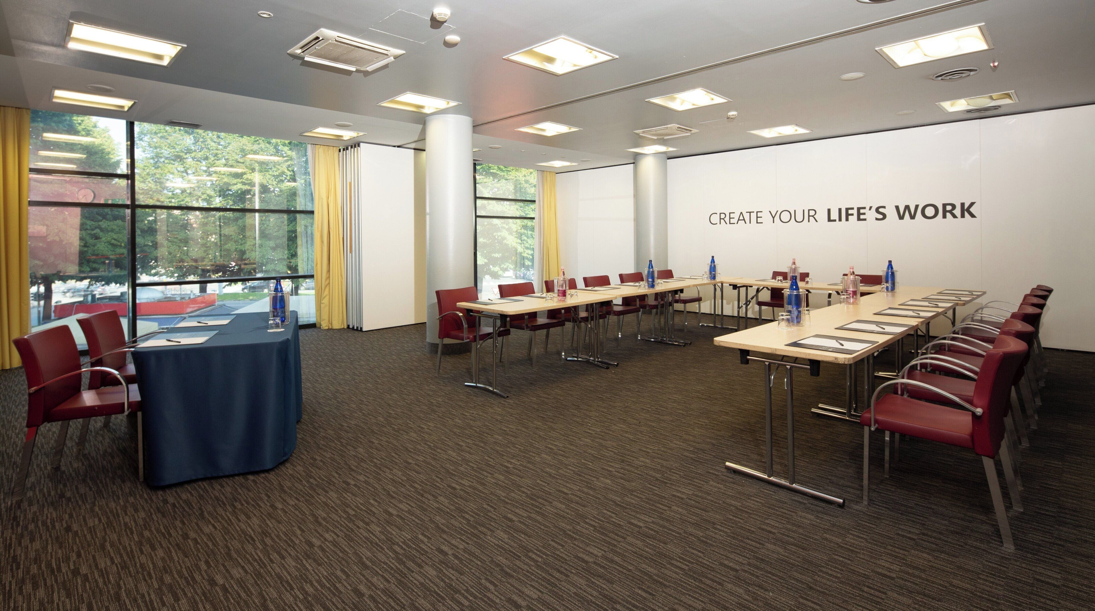 A conference room with a long table, red chairs, and a large window.
