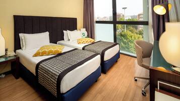 A hotel room with two beds, a desk, and a view of the city.