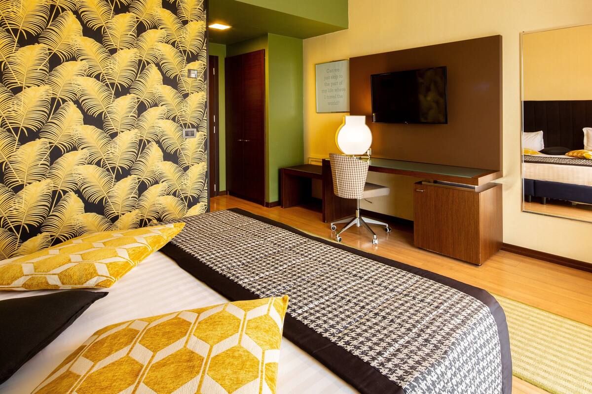 A hotel room with a bed, desk, chair, lamp, and a television.