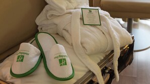 A hotel room with a neatly folded bathrobe and slippers with a green logo. - Holiday Inn Turin Corso Francia by IHG (Turin)