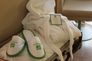 Een hotelkamer met een keurig opgevouwen badjas en slippers met een groen logo.