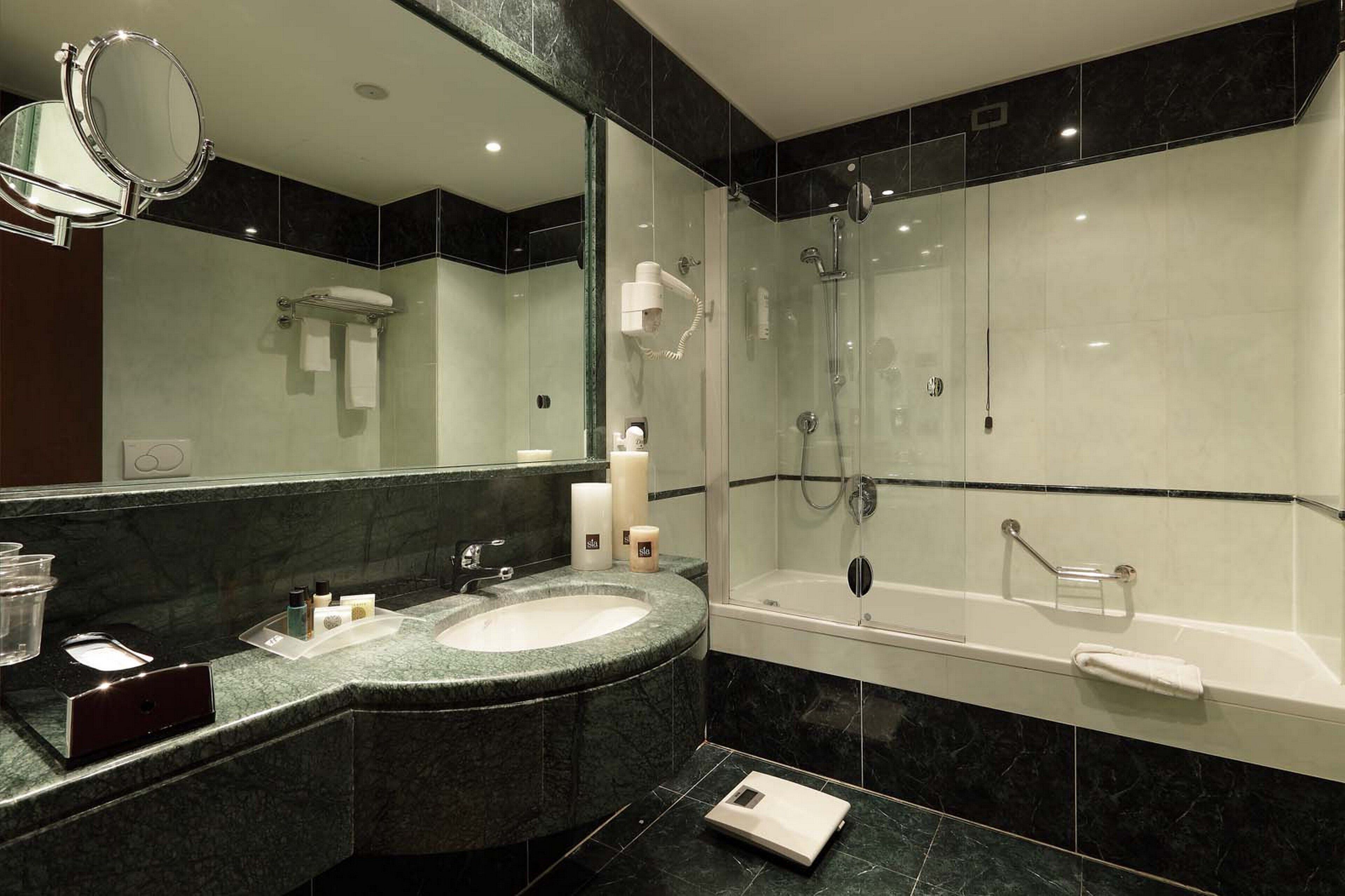 A modern bathroom with a marble sink, a large mirror, a glass-enclosed shower, and a bathtub.