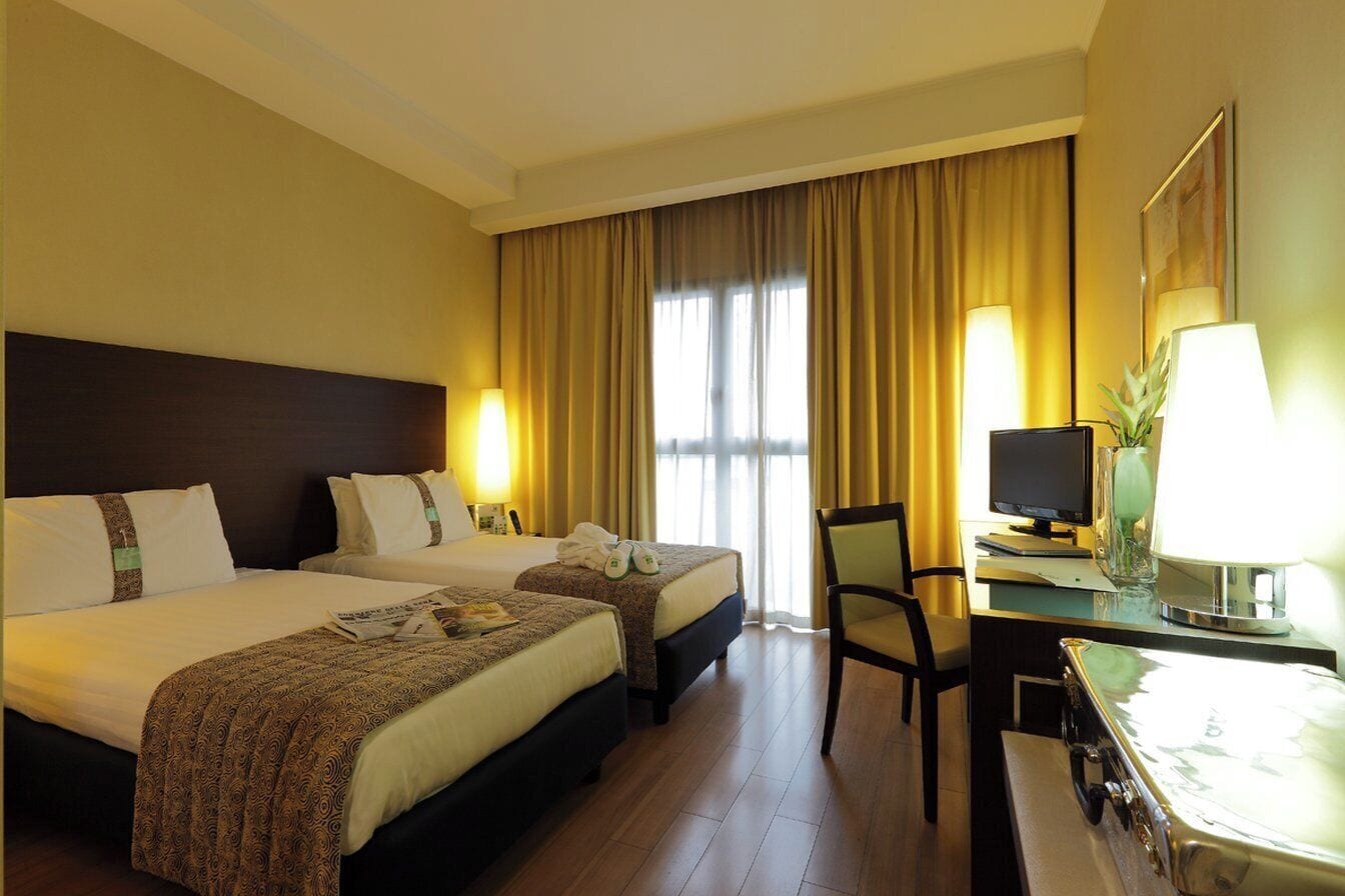 A hotel room with two beds, a desk with a computer, and a chair.