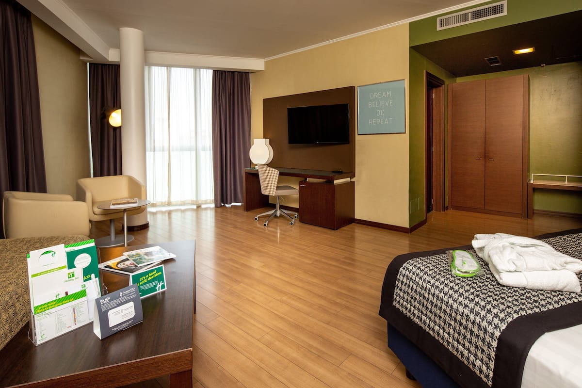 A hotel room with a bed, a desk, a chair, a TV, and a wardrobe.