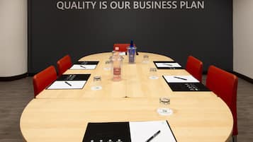 A conference room with a large table, red chairs, and a black screen with "QUALITY IS OUR BUSINESS PLAN" text.