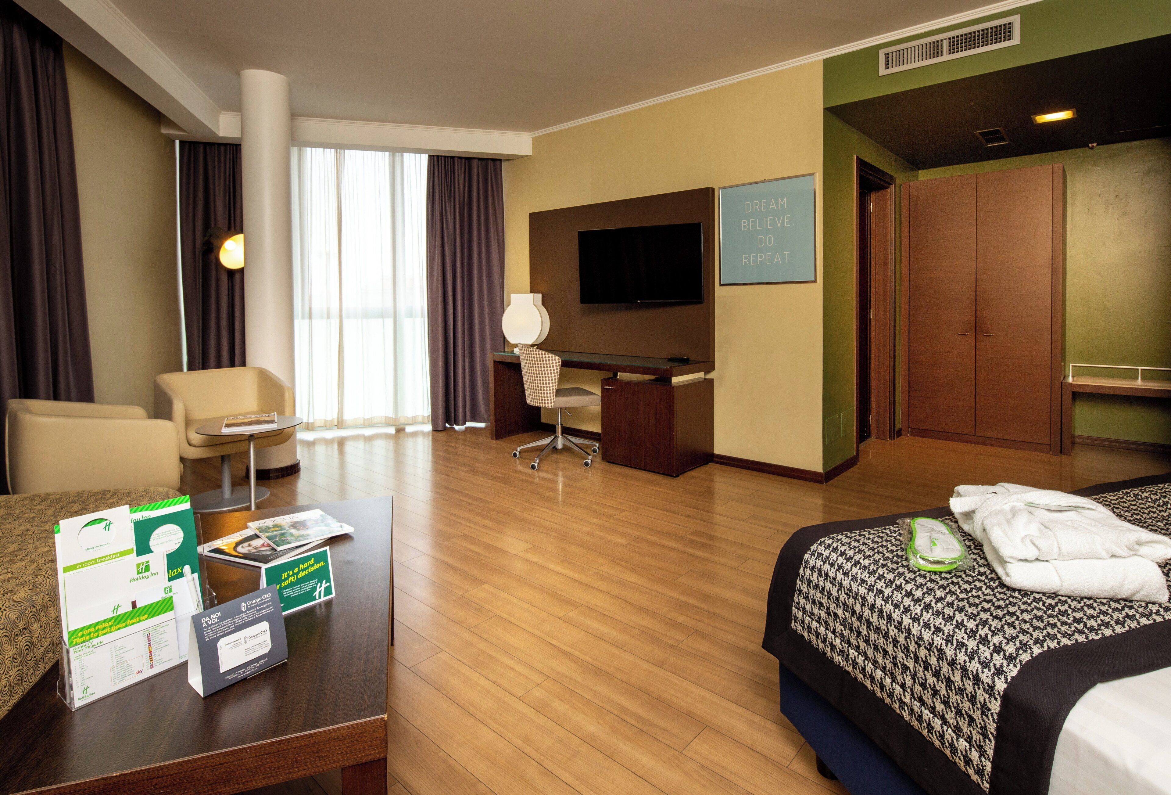 Une chambre d’hôtel équipée d’un lit, d’un bureau, d’une chaise, d’une télévision et offrant une vue sur l’extérieur.