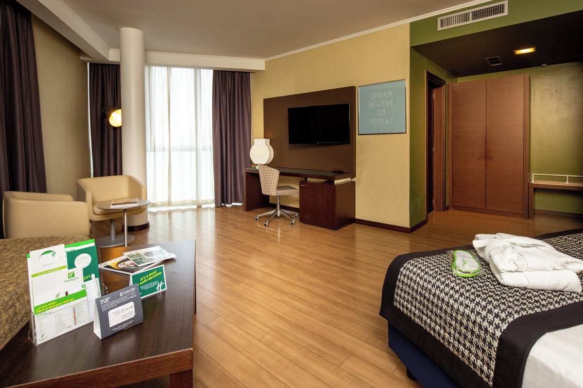 Een hotelkamer met een bed, bureau, stoel, televisie en uitzicht.