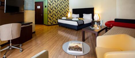 A hotel room with a bed, bedside table, lamp, and a magazine on a small table.