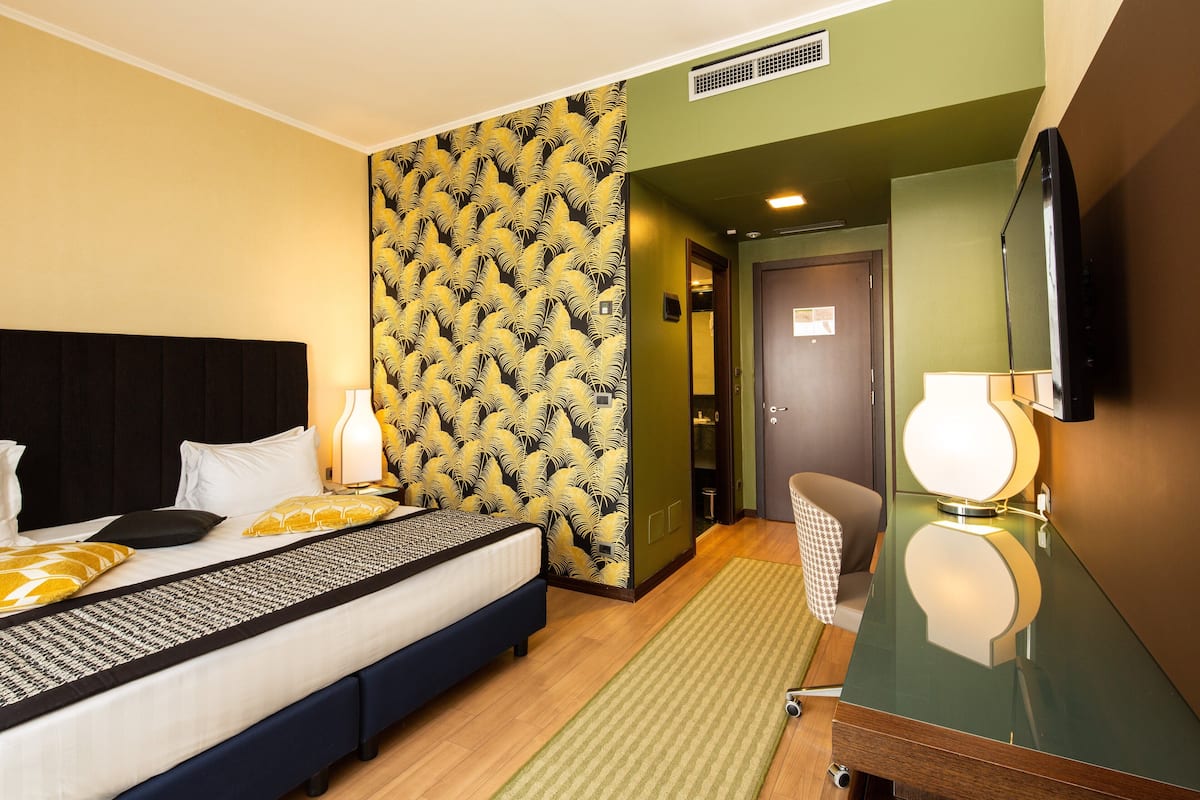 A hotel room with a bed, a mirror, a television, and a patterned wall.