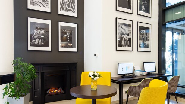 A modern interior with a fireplace, framed animal artwork, and yellow chairs. - Holiday Inn Turin Corso Francia by IHG (Turin)
