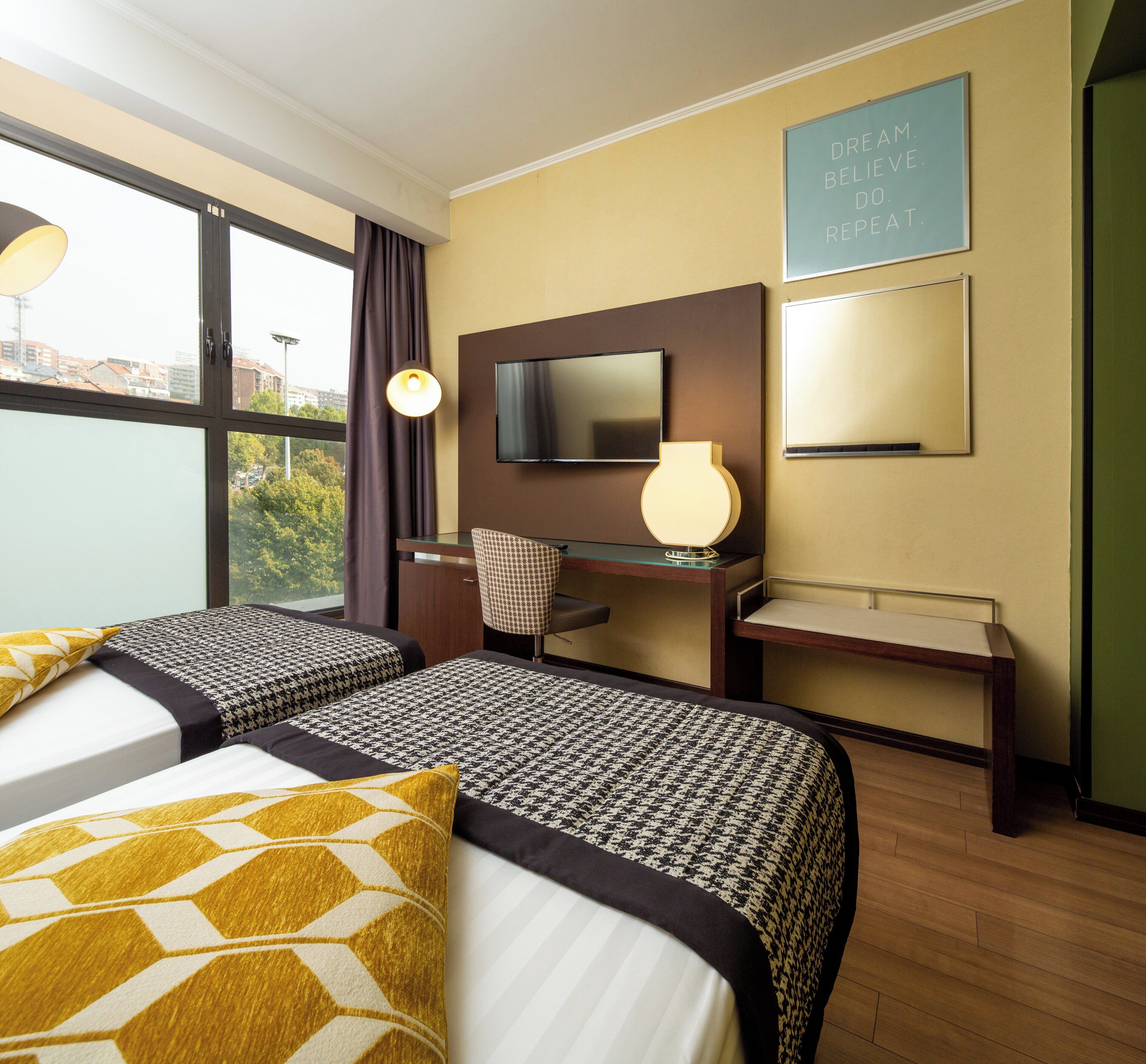 Een hotelkamer met twee bedden, een bureau, een stoel, een televisie en een raam met gordijnen.