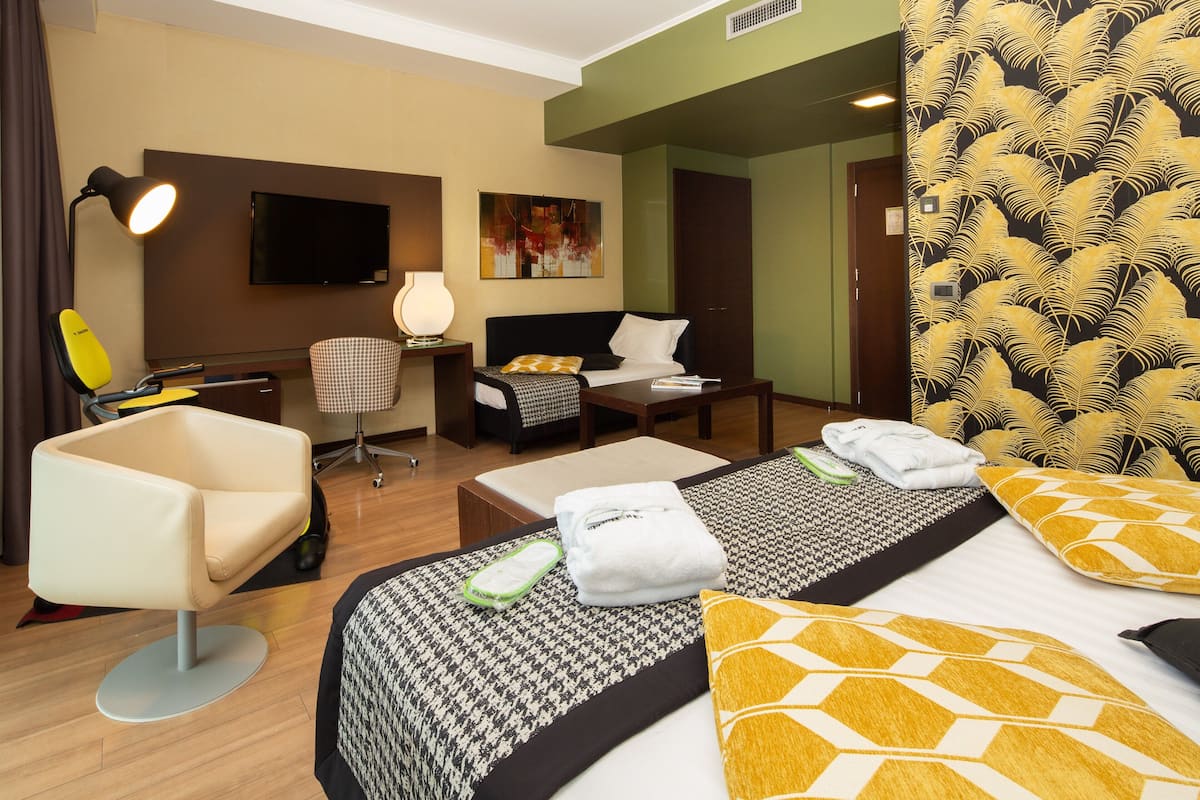 A hotel room with two beds, a desk, a chair, a TV, and a painting on the wall.