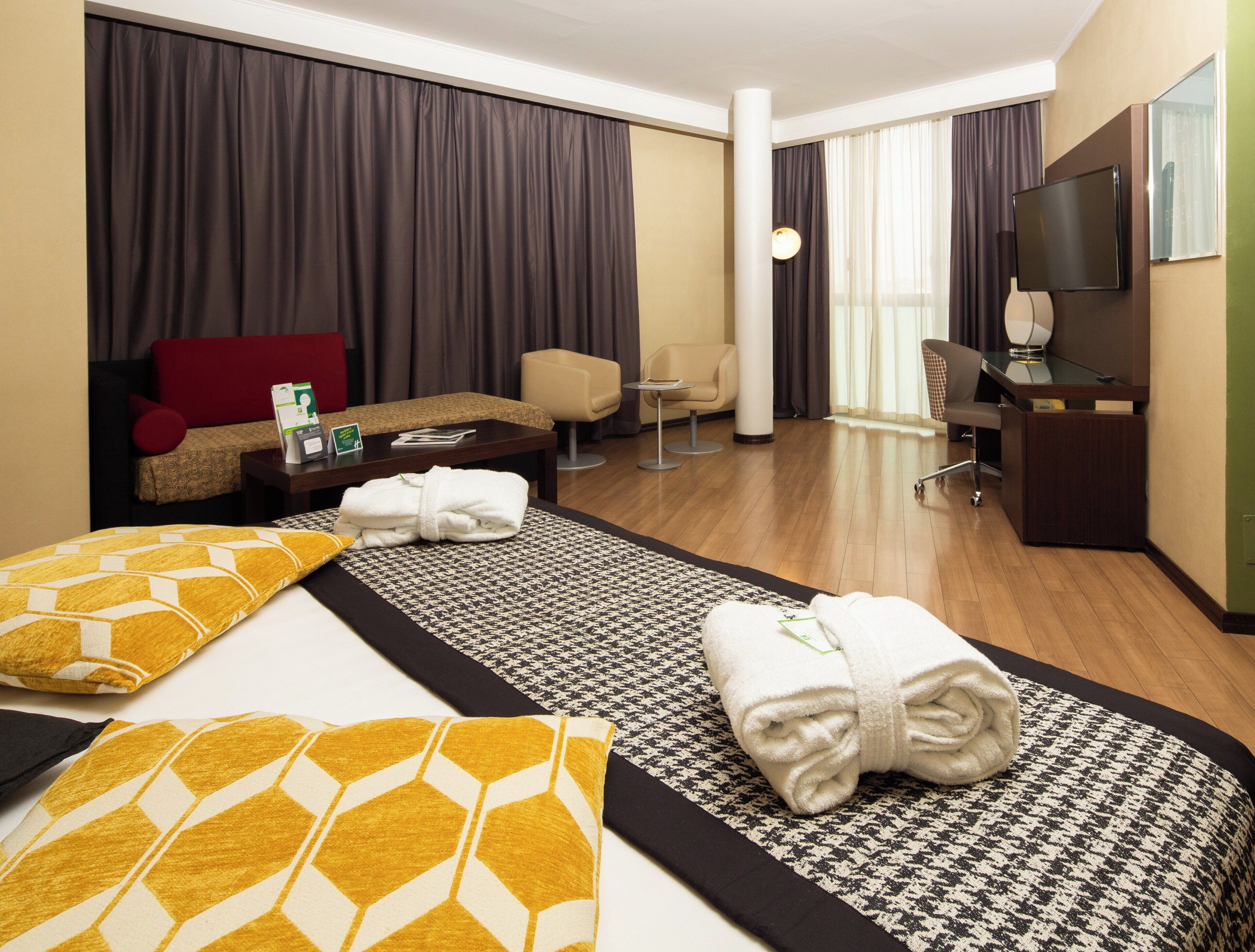 A hotel room with a bed, a desk, a chair, a sofa, and a TV.
