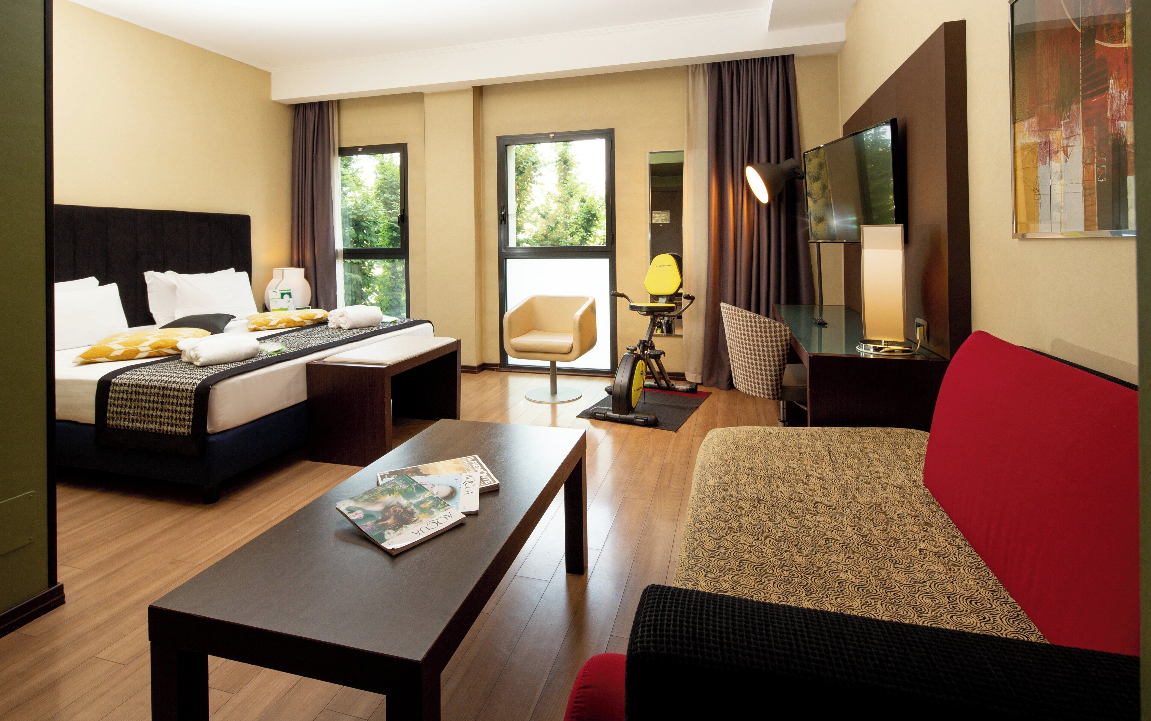 A hotel room with a bed, a desk, a chair, a sofa, and a window with curtains.
