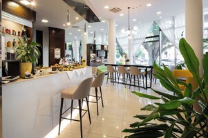 Zona bar moderna con un bancone bianco, sgabelli da bar e un'ampia scelta di cibi e bevande.