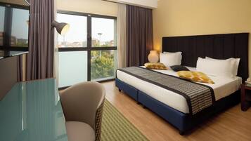 A hotel room with a bed, a desk, a chair, and a view of the city.