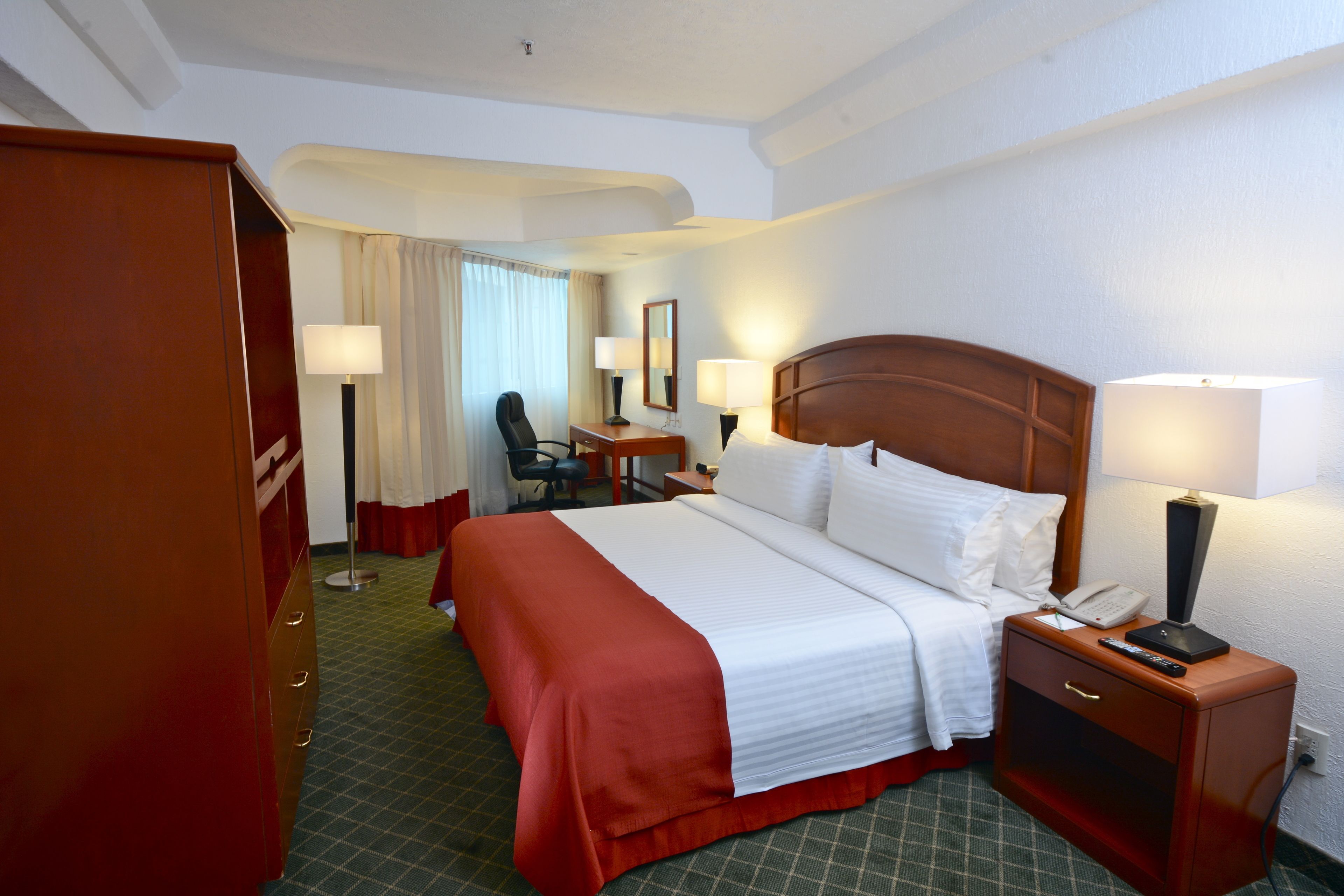 Una habitación de hotel con una cama grande, mesitas de noche, un escritorio y una silla.