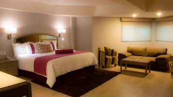 Una habitación de hotel con cama, mesita de noche, lámpara, sofá y sillón.