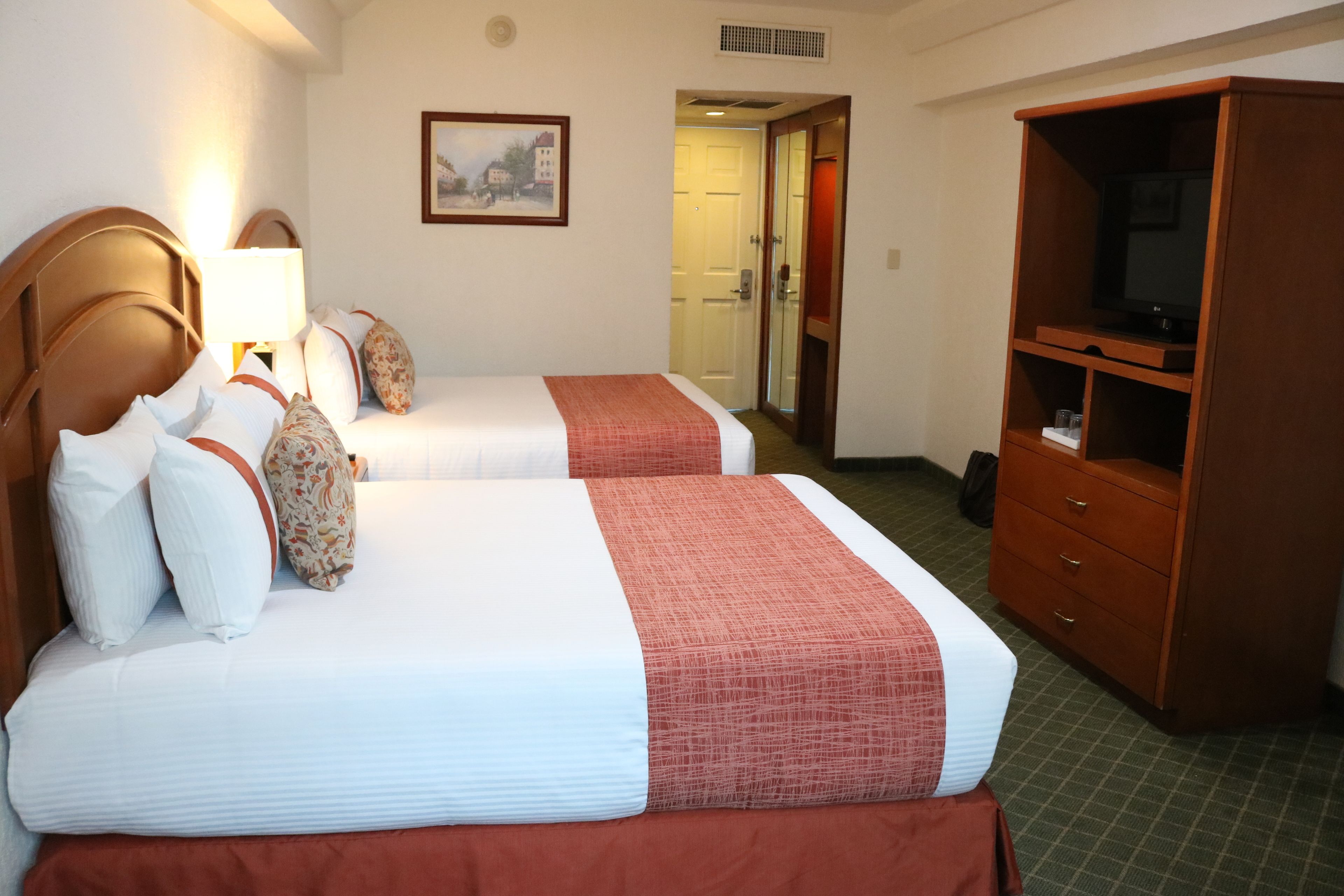 A hotel room with two beds, a television, a dresser, and a painting on the wall.