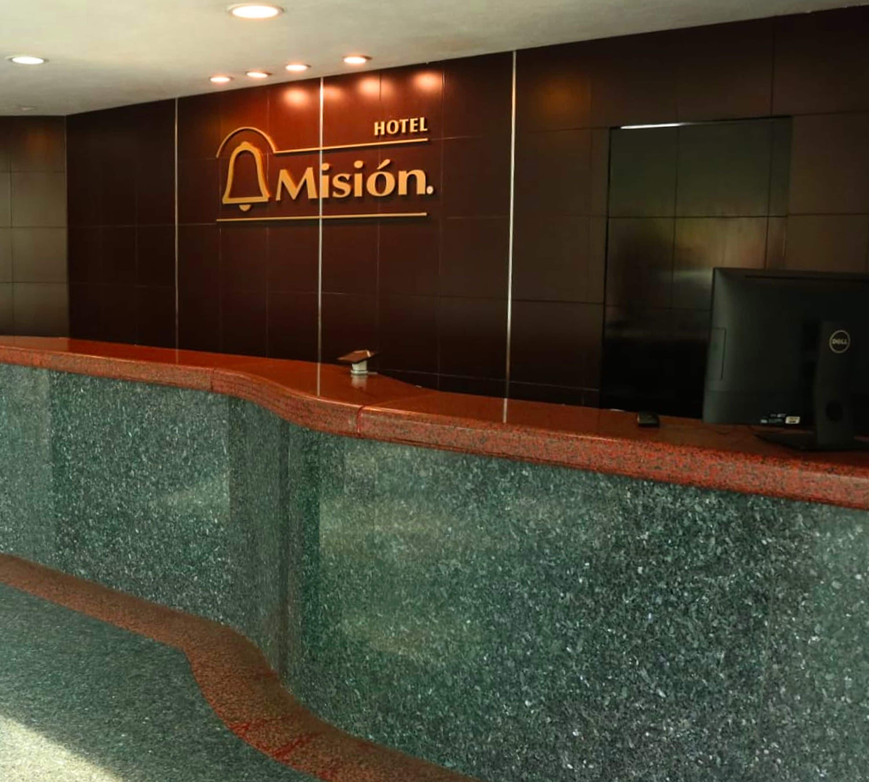 A reception desk with a dark wooden panel and a sign that reads "HOTEL Misión."