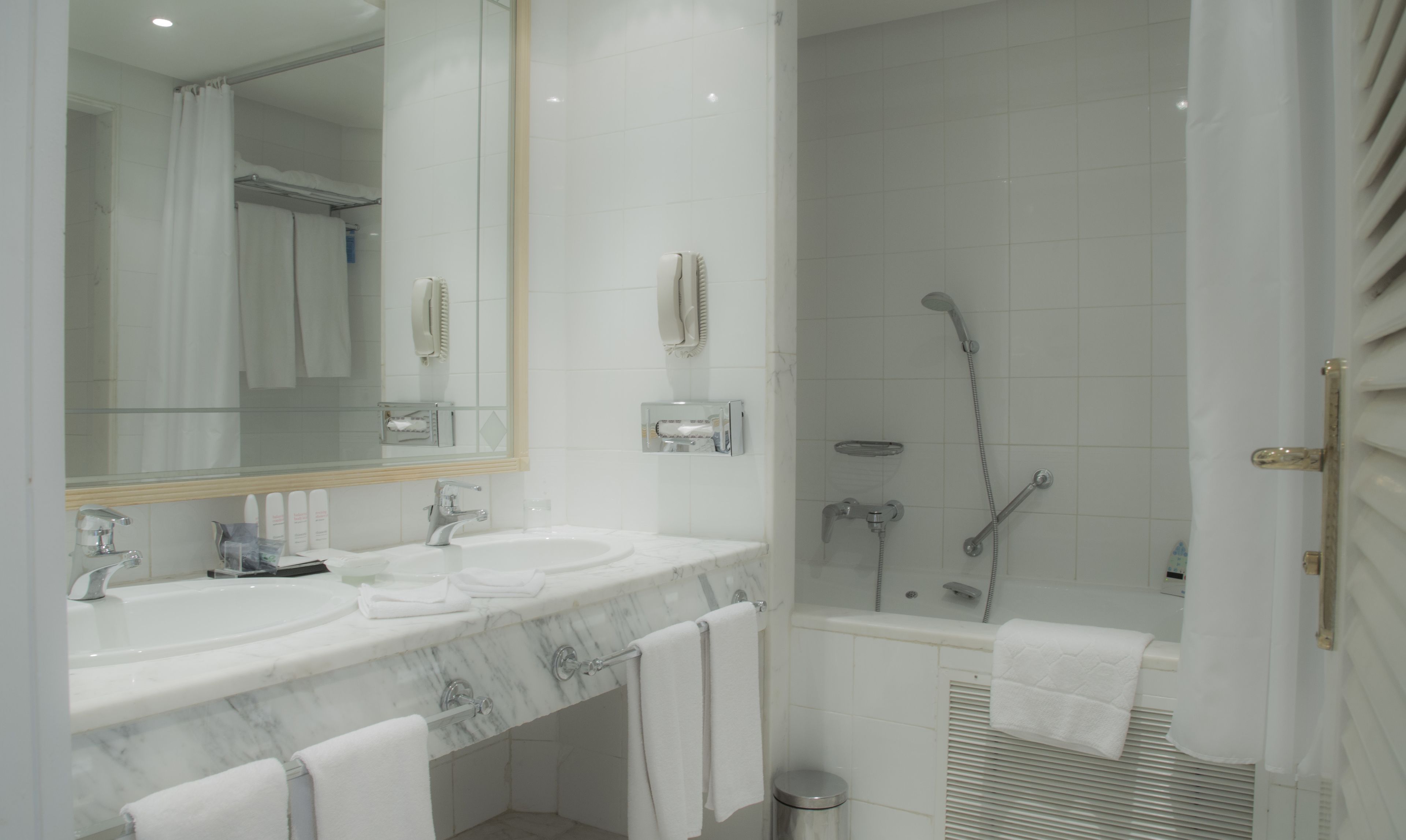A modern bathroom with two sinks, a large mirror, a shower with a handheld showerhead, and a towel rack.
