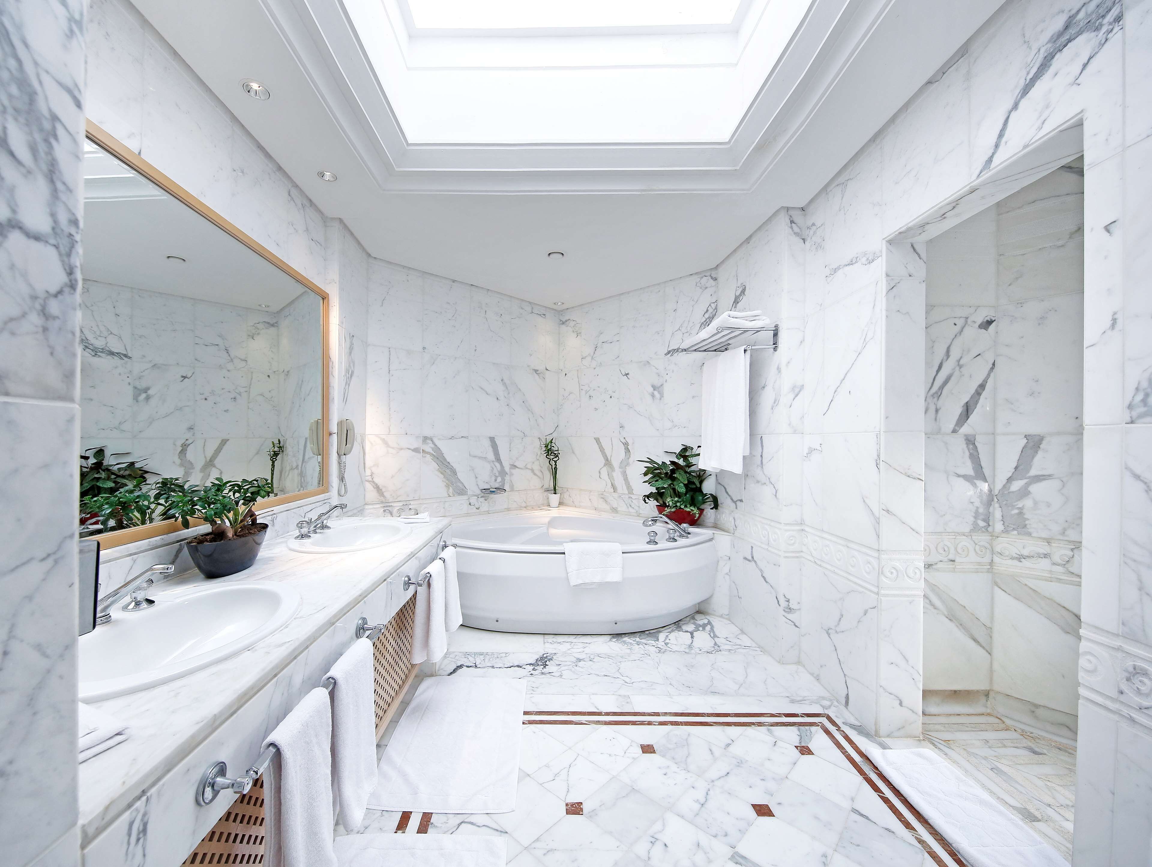 A luxurious bathroom with a skylight, marble walls, a large bathtub, and a separate shower area.