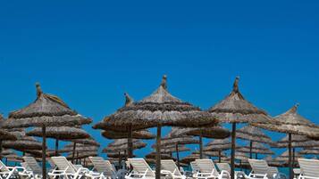 A beach with rows of white lounge chairs and thatched umbrellas.