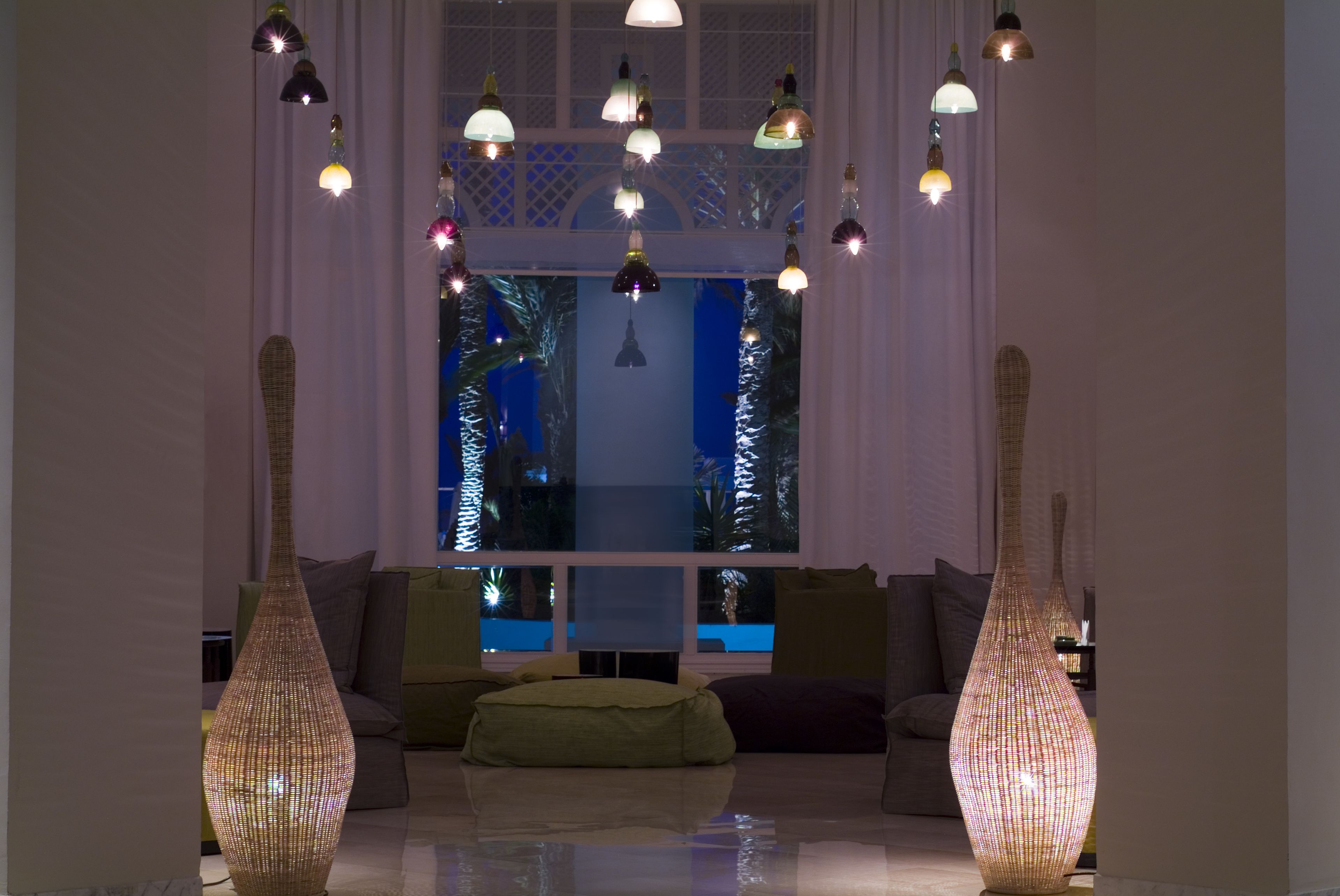 A modern living room with a large window, a sofa, a green pouf, and two tall, woven vases.