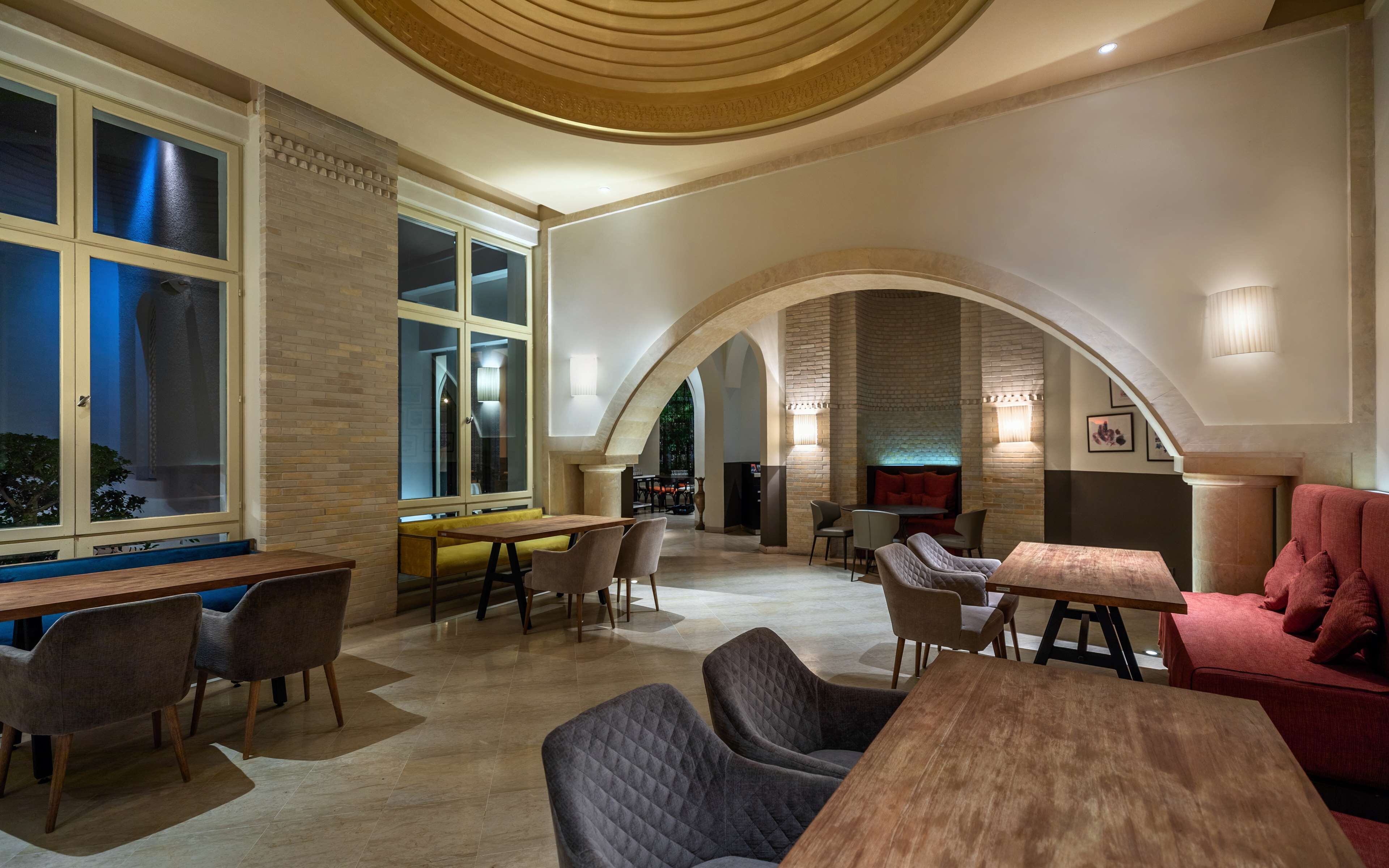 Un intérieur spacieux avec de hauts plafonds, des portes en arc de cercle et différents espaces de détente, comprenant des tables et des chaises.