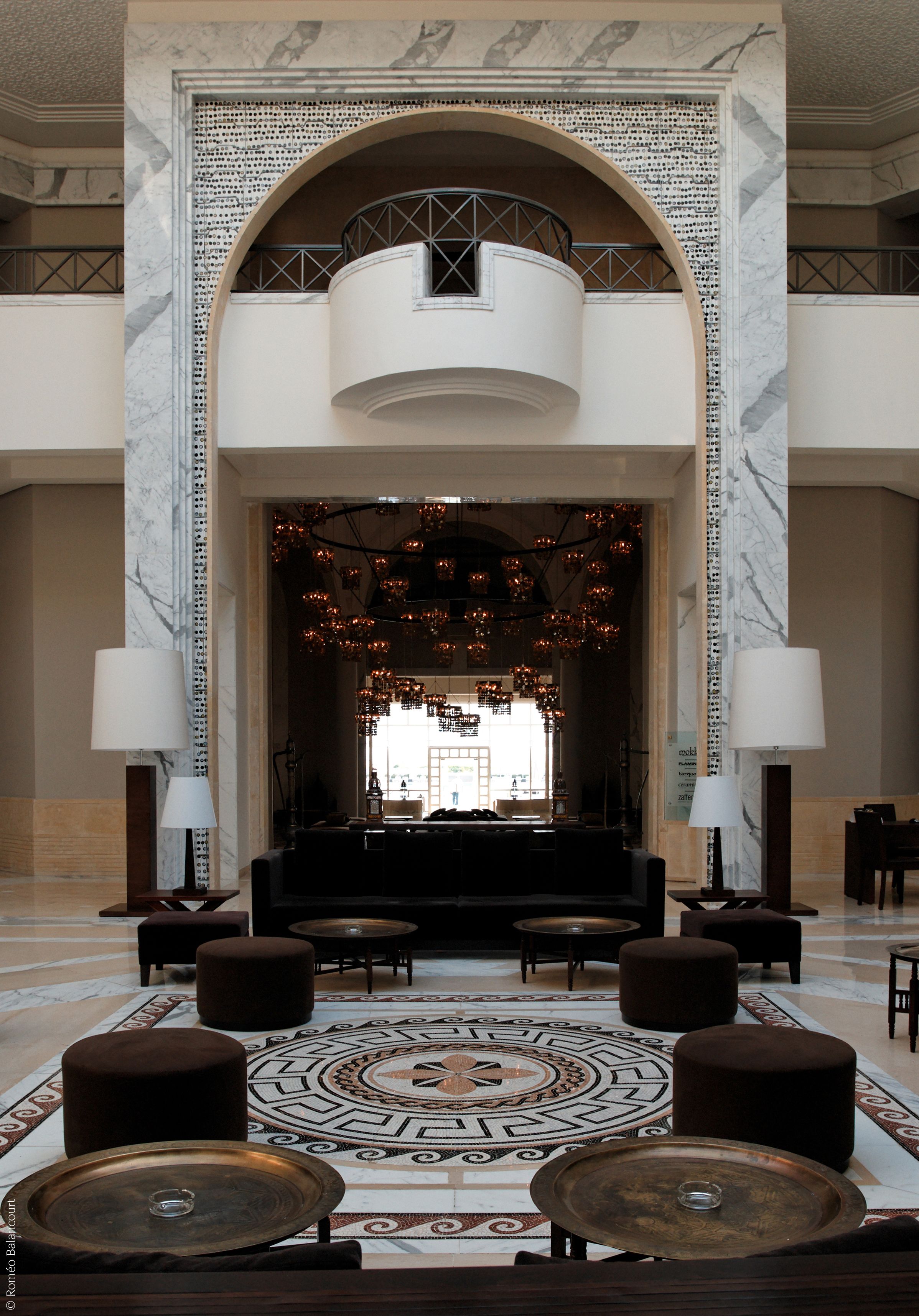 A lobby with a grand arched entrance, a central seating area, and a decorative chandelier.