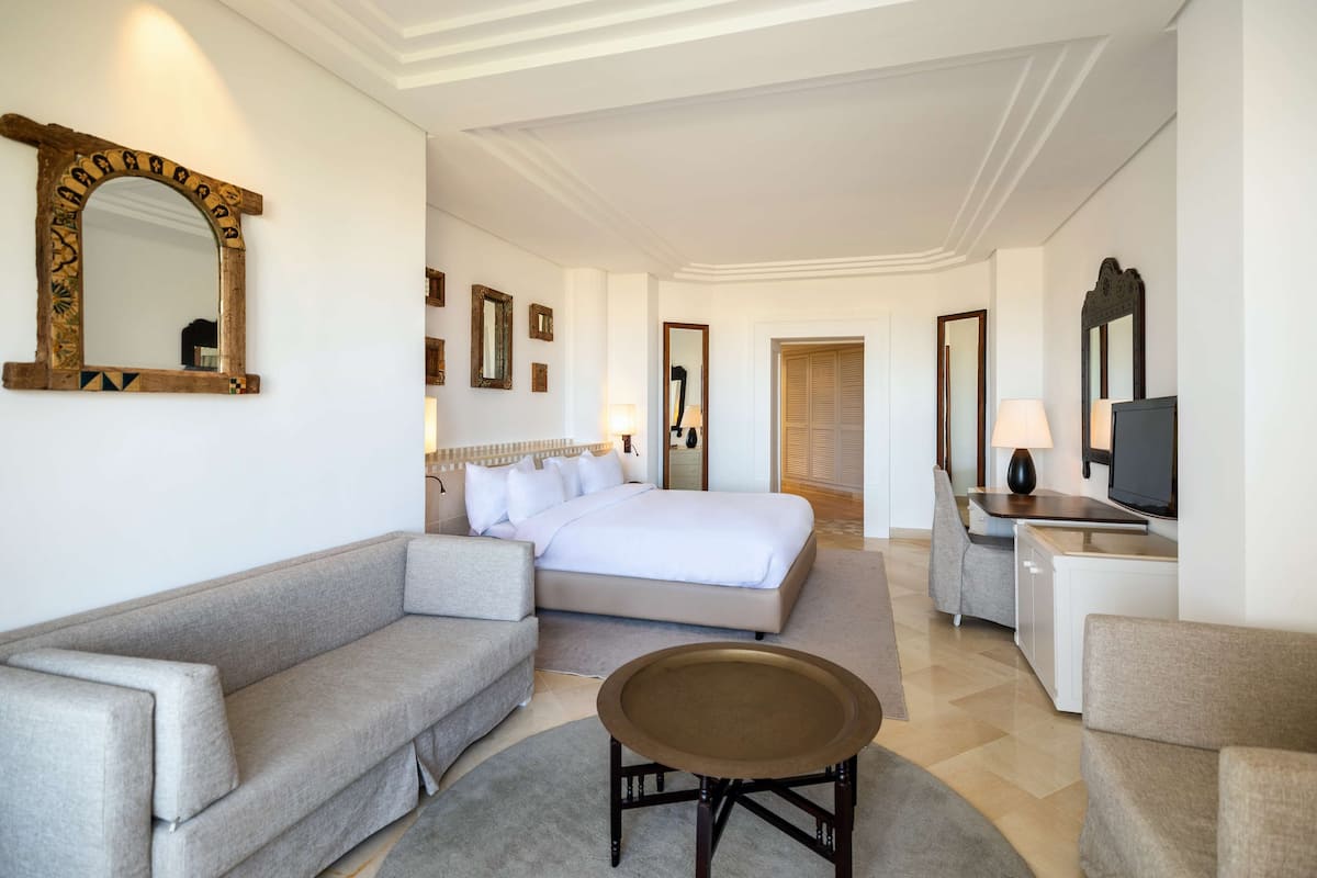 A hotel room with a bed, a sofa, a desk with a TV, and a mirror.