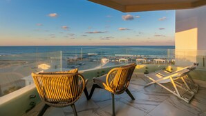 A balcony with two wicker chairs and a sun lounger overlooking a beach with boats and umbrellas. - Radisson Blu Athénée Palace Resort & Thalasso, Djerba (Mezraia)
