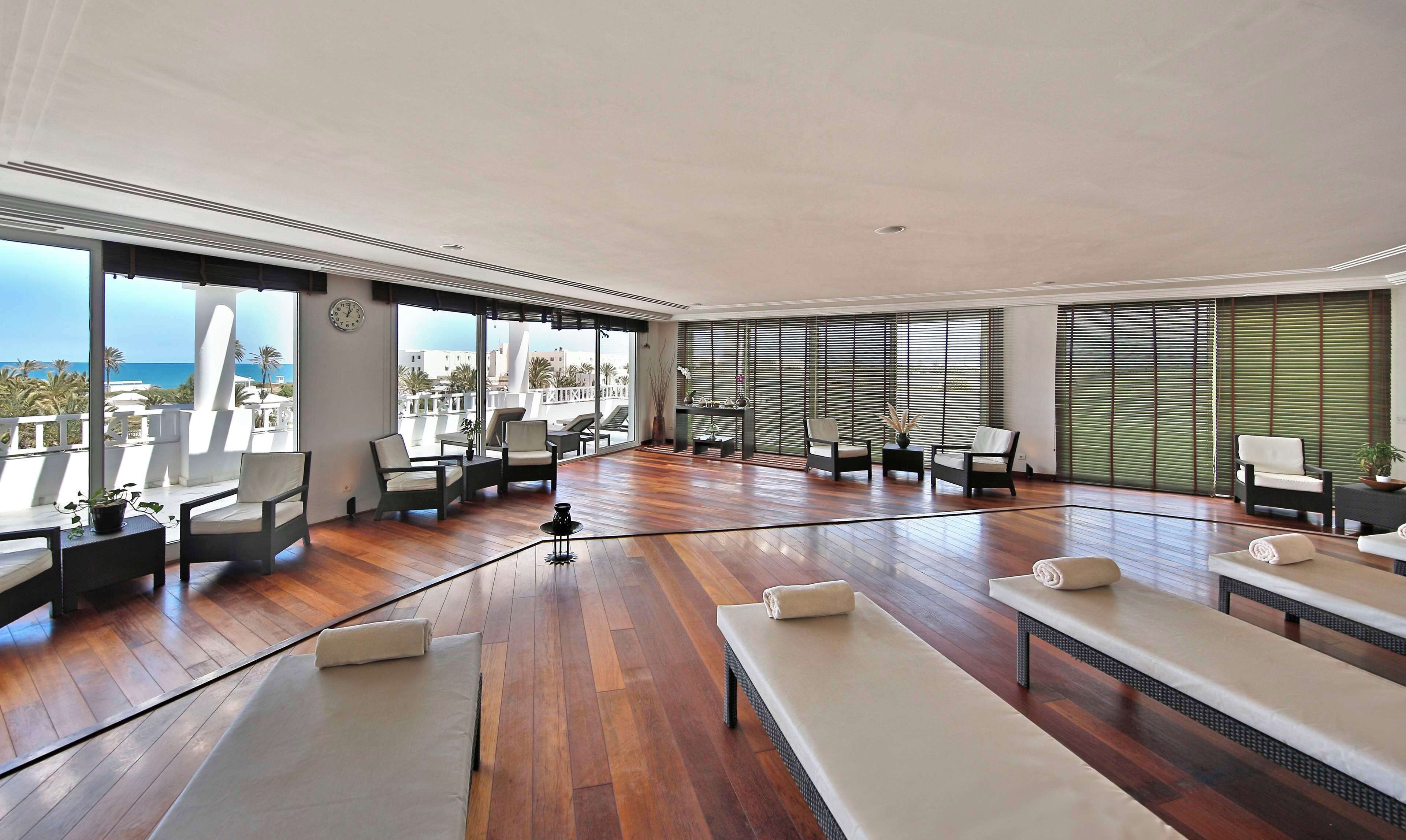 A spacious room with wooden flooring, multiple seating areas, and large windows offering ocean views.