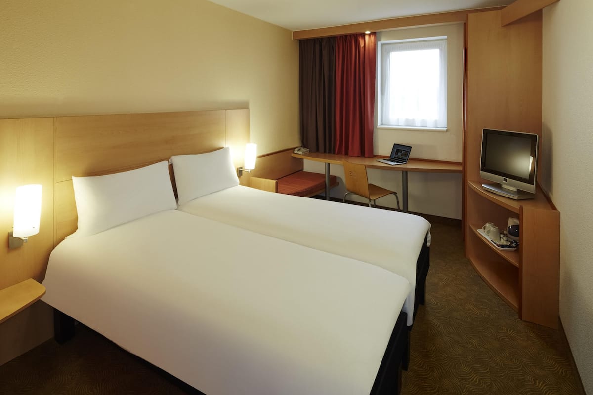 Hotellihuone, jossa on suuri sänky, työpöytä tietokoneella, televisio ja pieni oleskelualue.