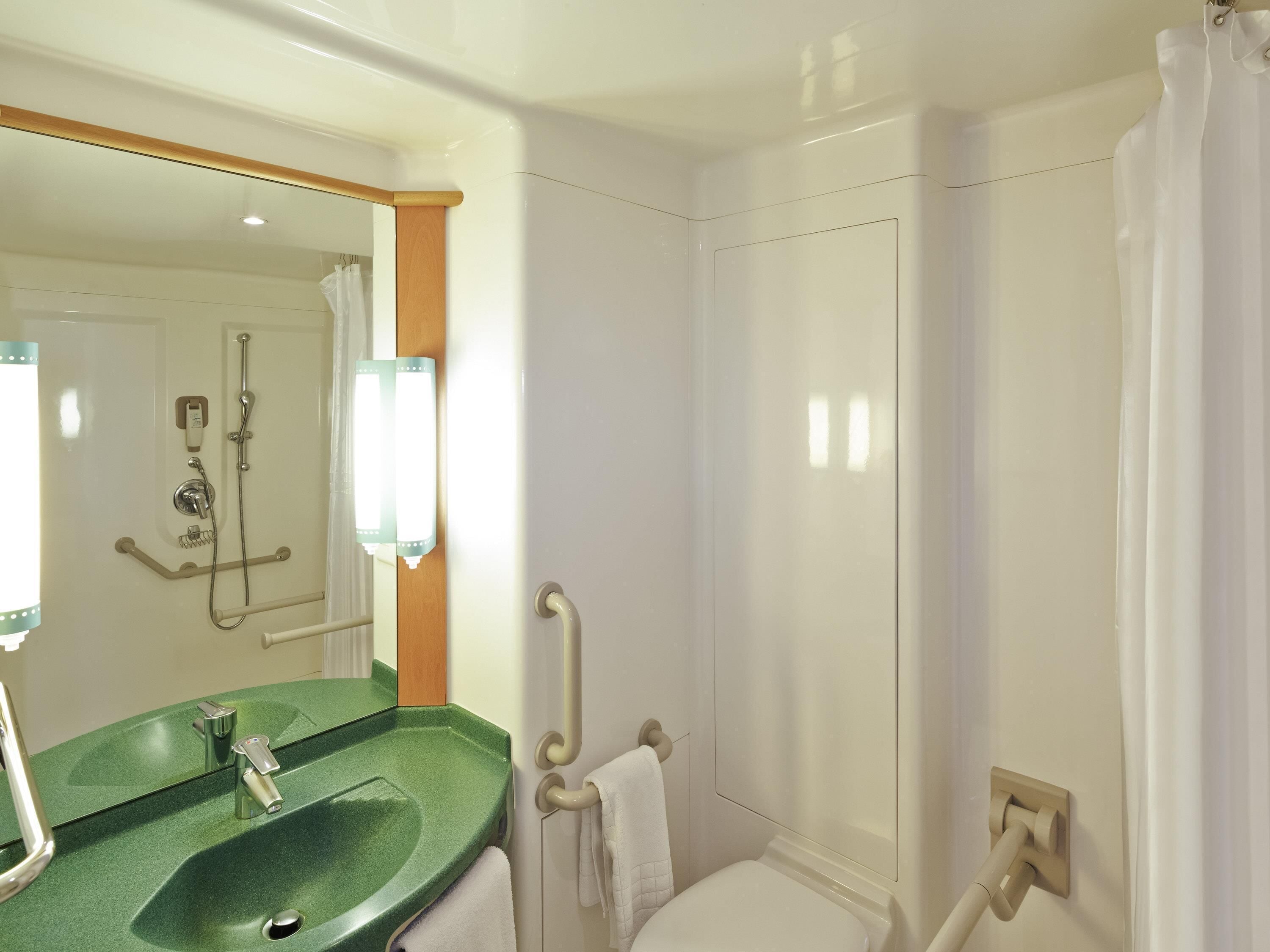 A bathroom with a green sink, a mirror, a shower, and a toilet.