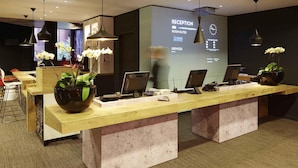 Een receptiebalie met een digitaal scherm, een kamerplant en een modern interieur.