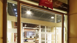 De ingang van een ibis hotel met een receptiebalie, glazen deuren en een bord boven de ingang.
