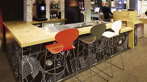 Een bar met een houten toonbank, barstoelen en een wand met een patroon.