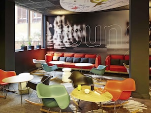 A modern lounge area with a red sofa, colorful chairs, and a large wall mural. - ibis Reading Centre (Reading)