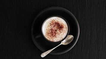 Una taza de café con una cuchara sobre un platito negro.
