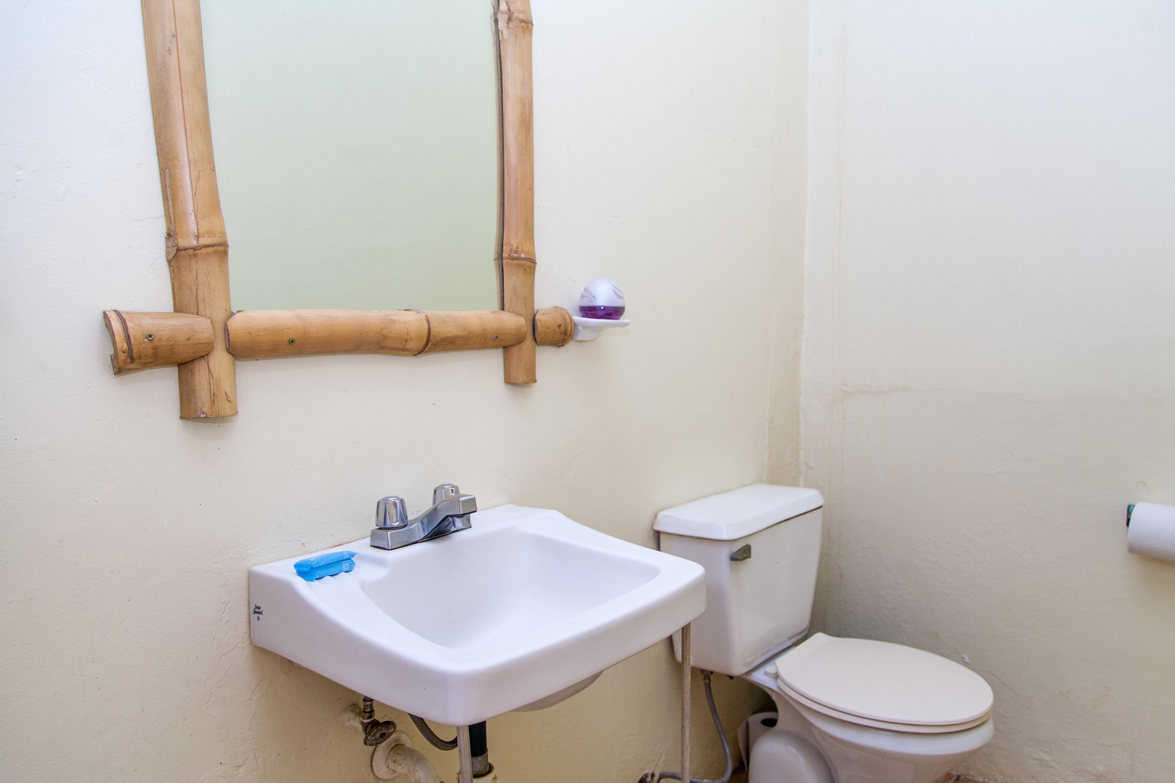 Un baño con un lavamanos blanco, un inodoro y un espejo con marco de bambú.