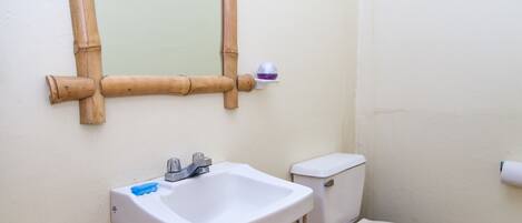A bathroom with a white sink, a toilet, and a mirror with a bamboo frame.