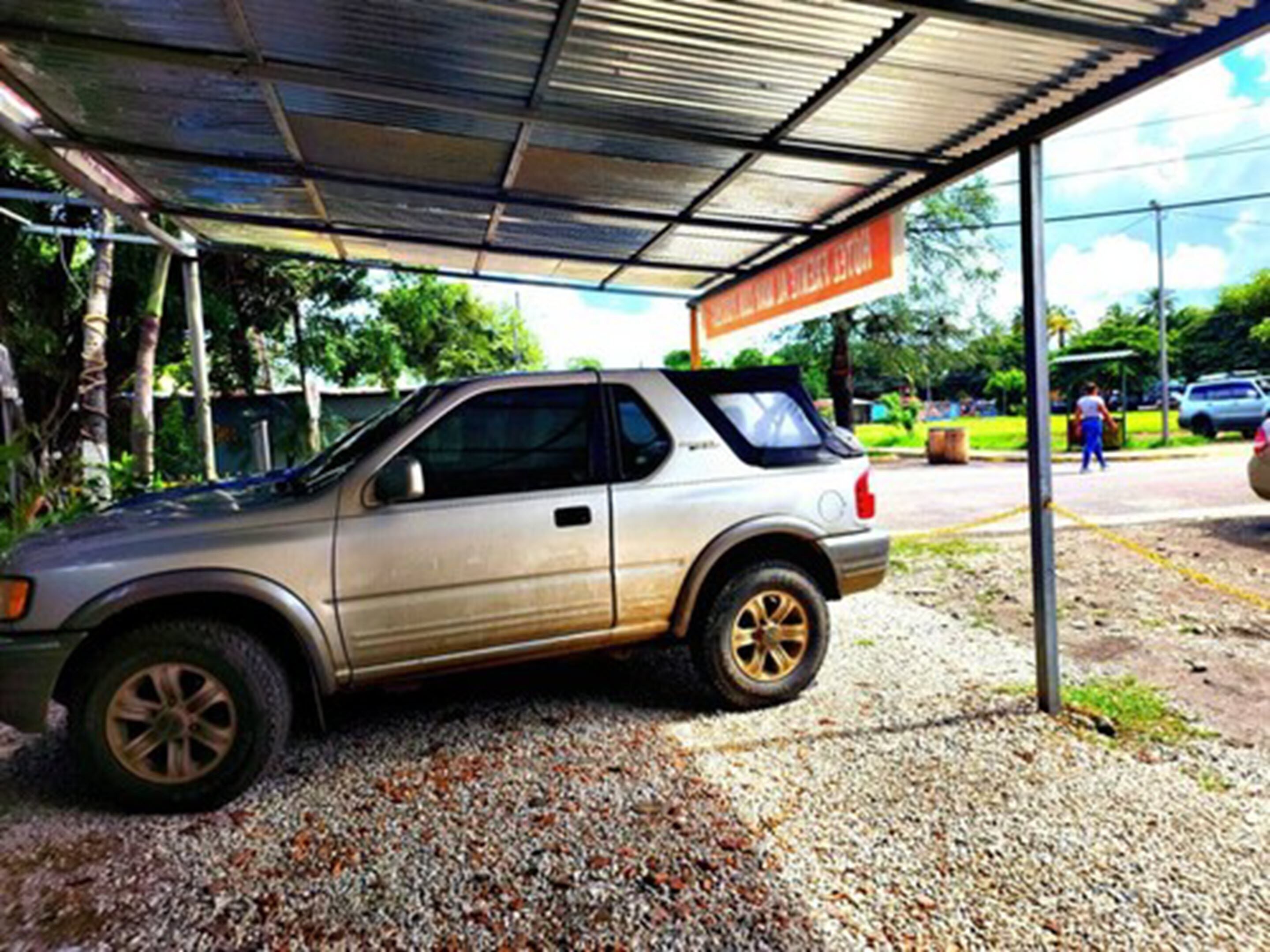 Un coche estacionado bajo una zona cubierta con un cartel al fondo.