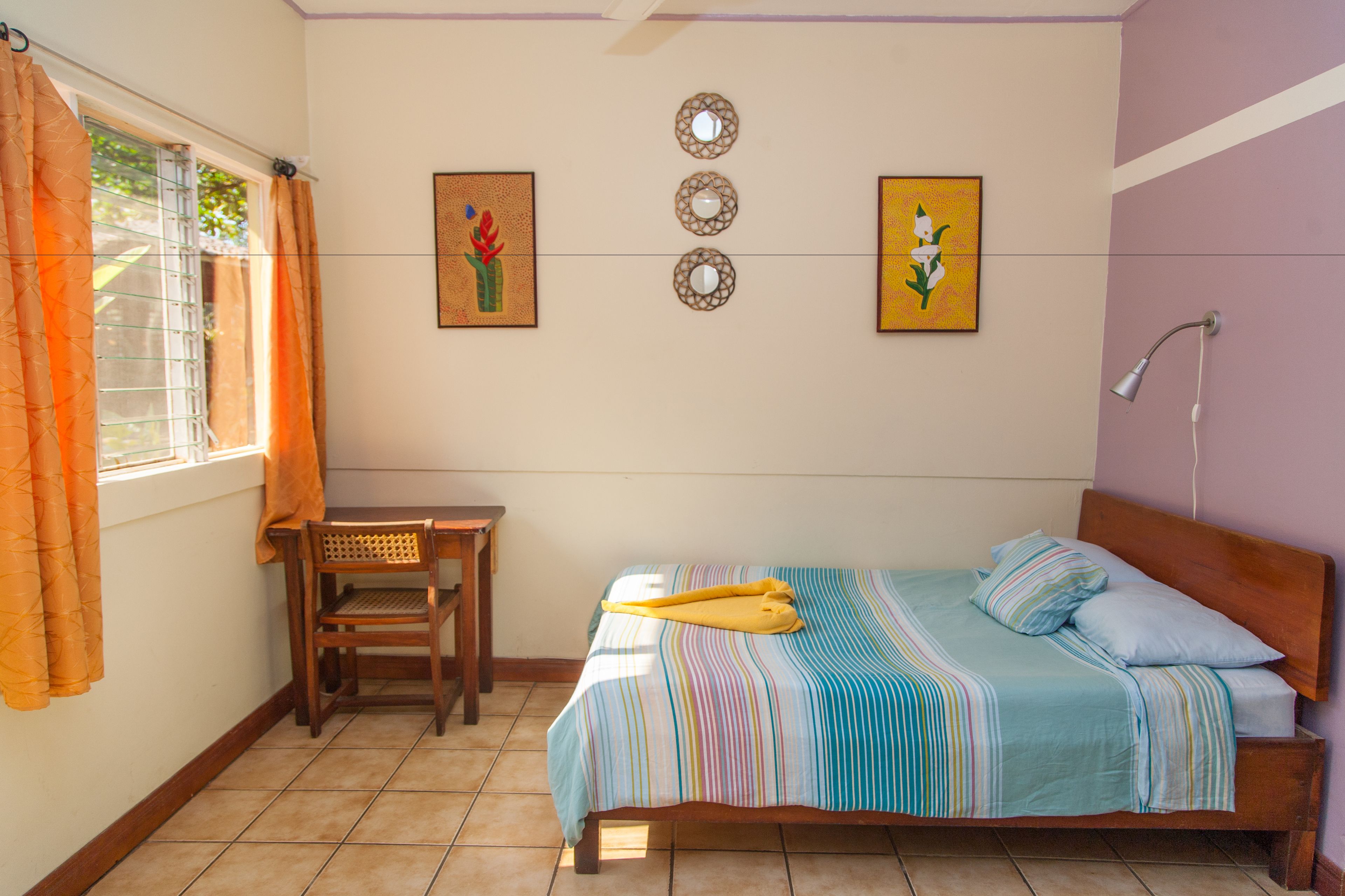 Un dormitorio con cama, una silla, una mesa y una ventana con cortinas.