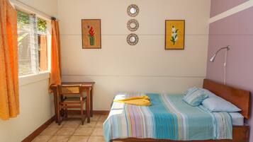 Un dormitorio con cama, una silla, una mesa y una ventana con cortinas.