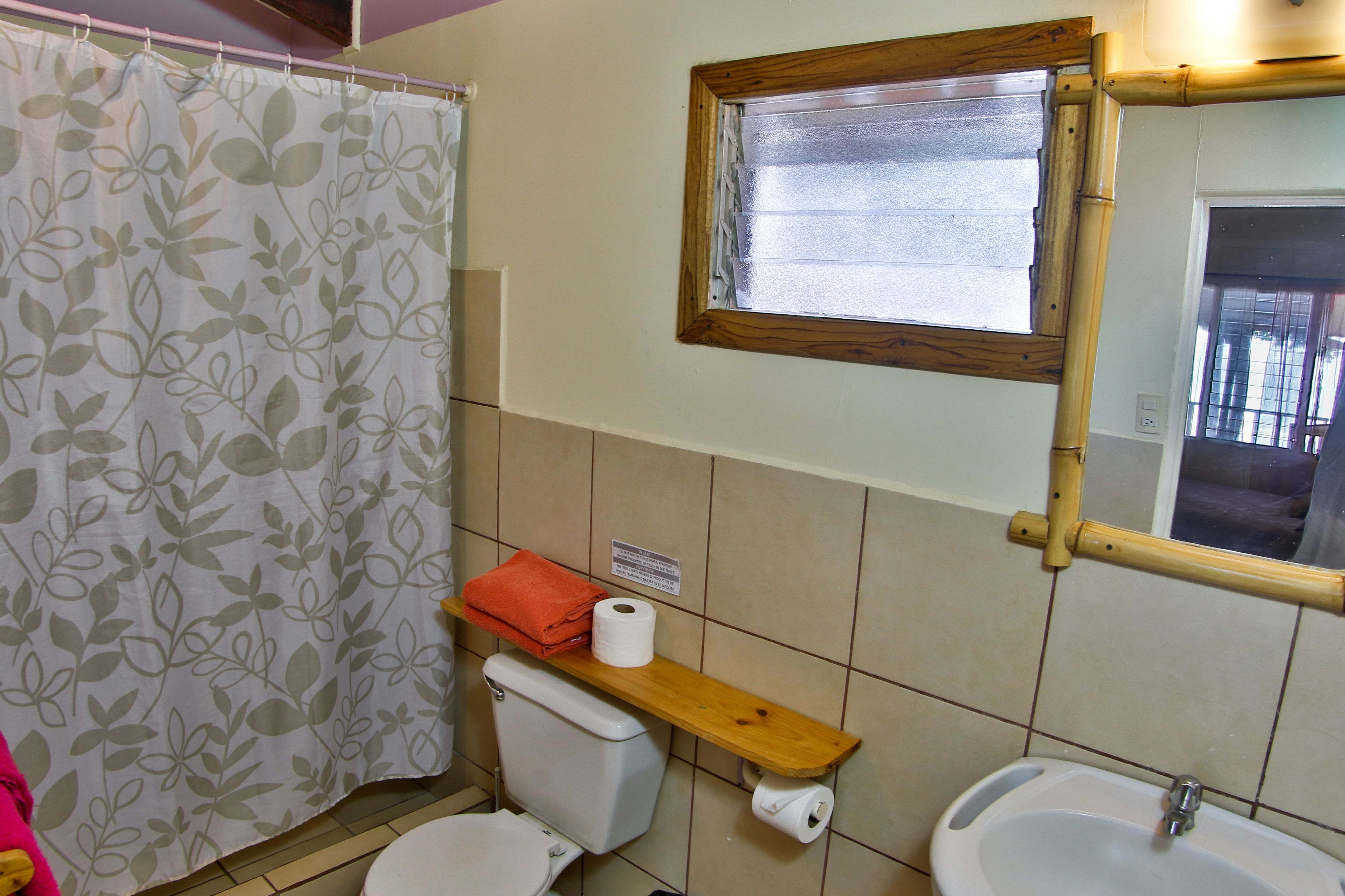 A bathroom with a toilet, a sink, a shower curtain, and a window with a wooden frame.