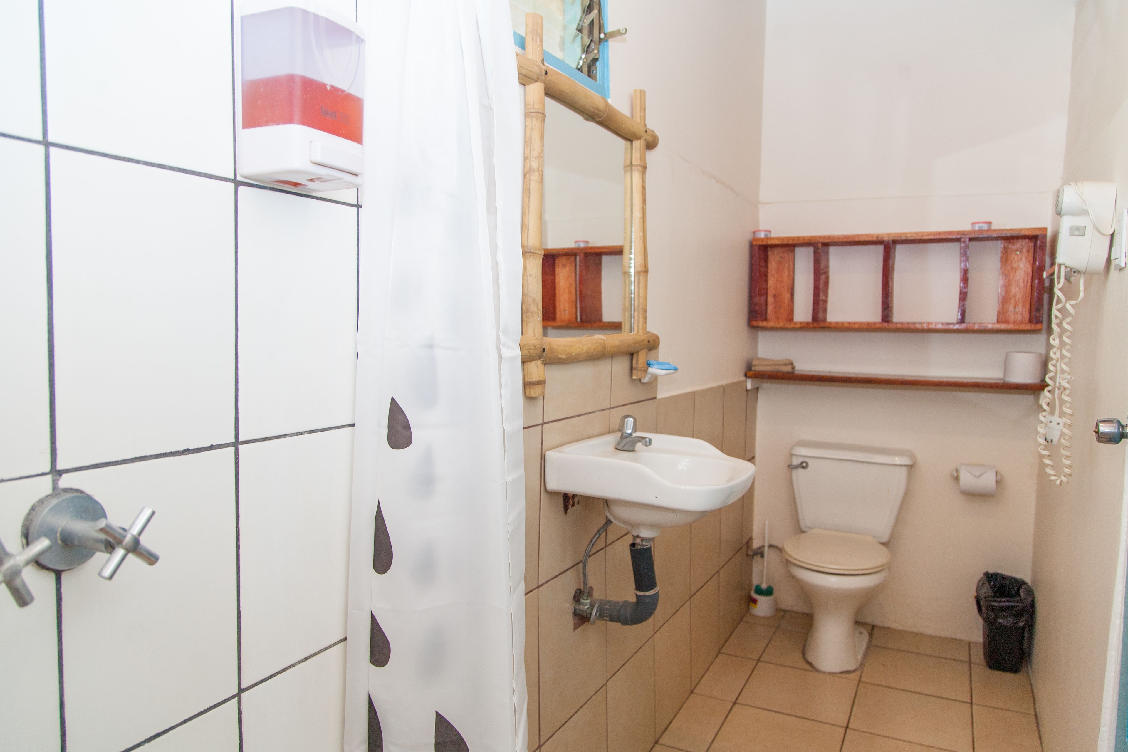 Un baño con un lavamanos blanco, un inodoro, una cortina de ducha y un estante de madera sobre el inodoro.