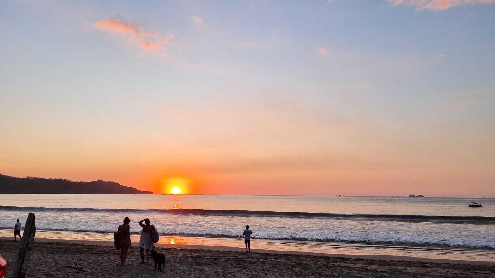 Escena de playa con gente y un atardecer.